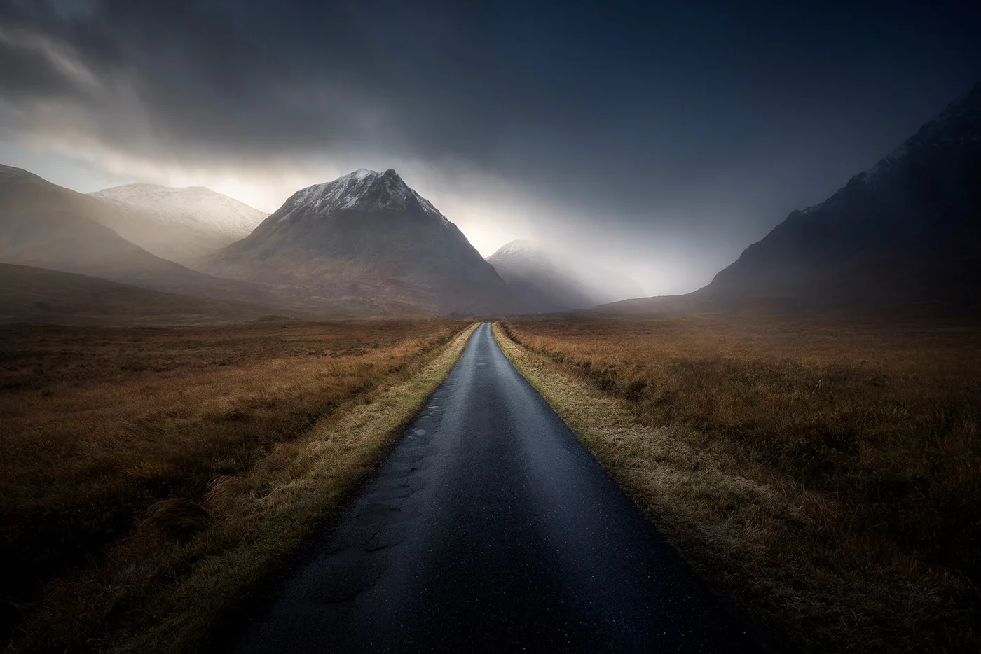 Route droite menant vers une montagne sous un ciel orageux, photographiée par Aliaume Chapelle