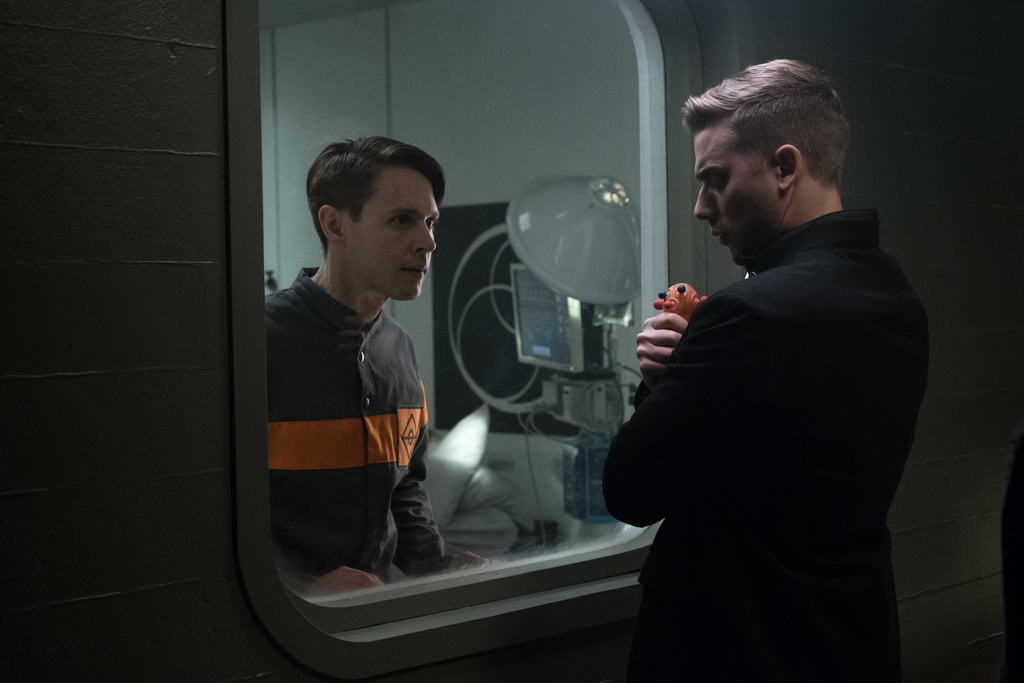 Dirk Gently observé à travers une vitre dans les installations de Blackwing